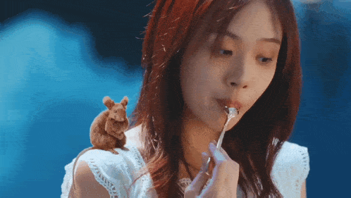 a woman is eating a piece of food with a mouse sitting on her shoulder