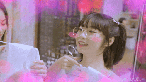 a girl wearing glasses and a ponytail is smiling and looking at something