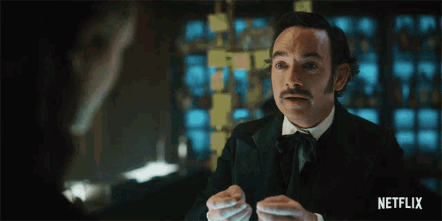 a man with a mustache is talking to a woman with a netflix logo in the corner