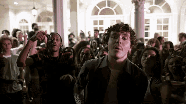 a man with curly hair is standing in front of a crowd