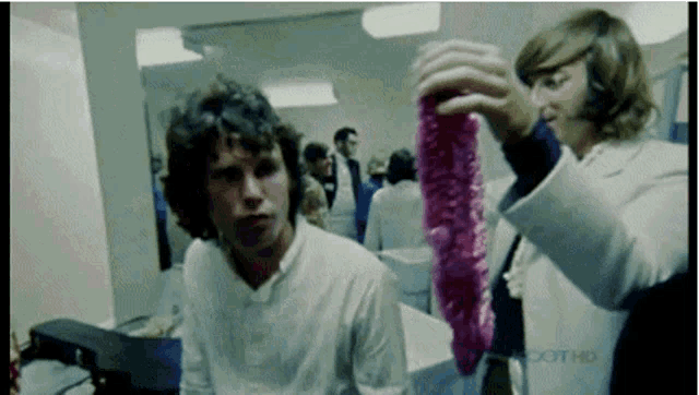 a man and a woman are standing next to each other in a room and the woman is holding a pink object .