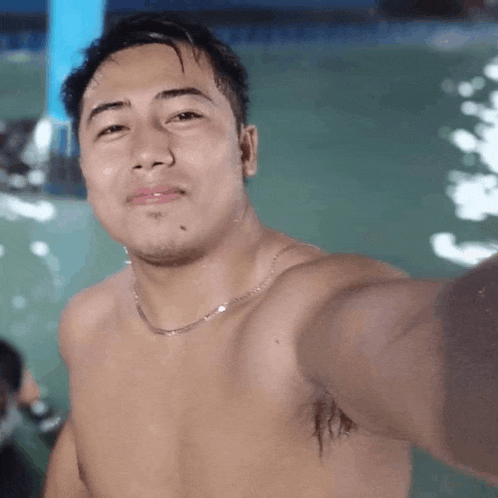 a shirtless man is taking a selfie in front of a swimming pool