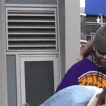 a man wearing a purple shirt that says los angeles is standing in front of a window .