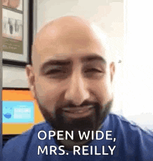 a man with a beard is smiling and saying `` open wide , mrs. reilly '' .