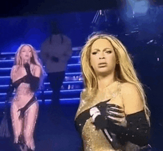 a woman is holding a microphone on a stage while another woman sings behind her .