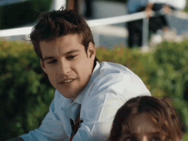 a man in a white shirt and tie is sitting next to a woman in a park .