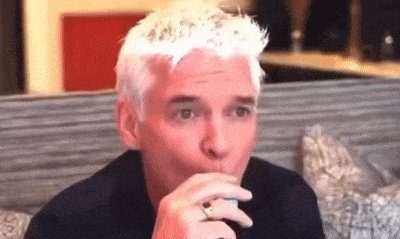 a man with white hair and a ring on his finger is sitting on a couch eating a sandwich .