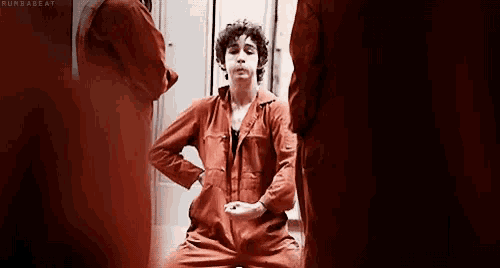 a man in a red jumpsuit is sitting with his hands on his knees