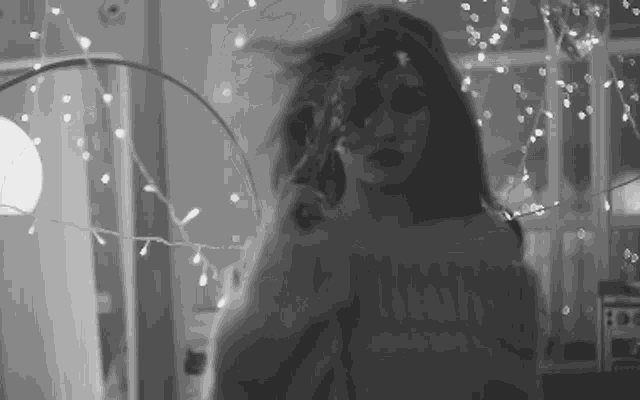 a woman in a sweater is standing in front of a lamp and christmas lights .