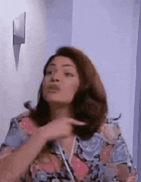 a woman in a floral shirt is pointing at her hair and making a funny face .