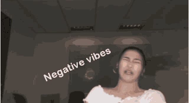 a woman is making a funny face with her fist in the air and the words `` negative vibes '' written on her face .