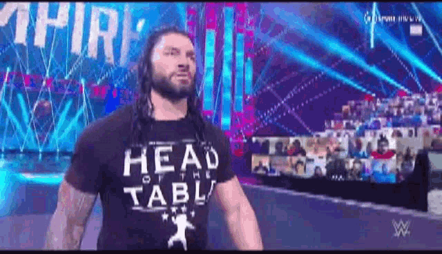 roman reigns is wearing a head of the table t-shirt while walking on the stage .