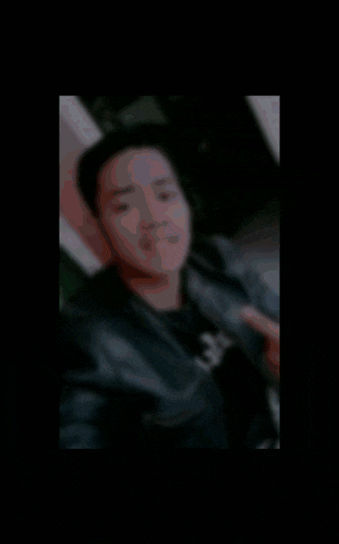 a man in a leather jacket is taking a selfie with the letter b in the corner