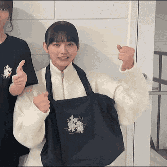 a girl is holding a black bag and giving a thumbs up sign