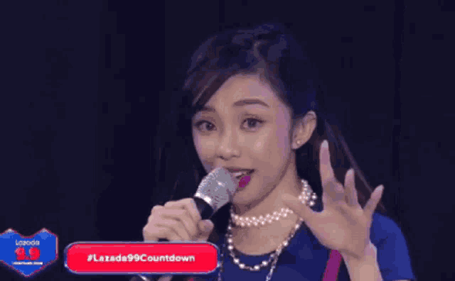 a woman is holding a microphone in front of a screen that says # lazada99countdown