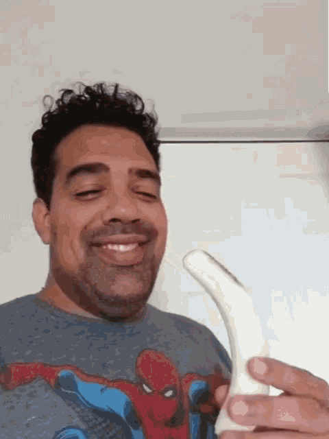 a man wearing a spider man shirt is holding a white object