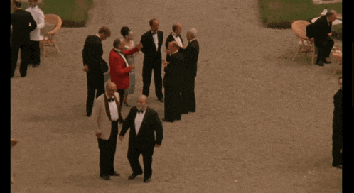 a group of men in tuxedos are standing on a gravel driveway