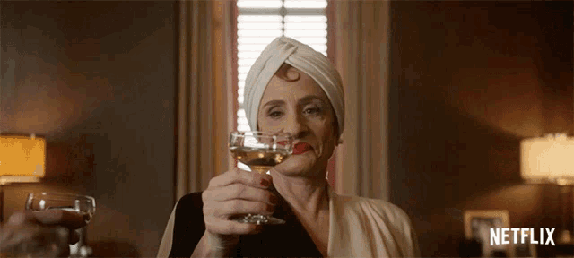 a woman in a white turban is holding a glass of wine and a glass of water