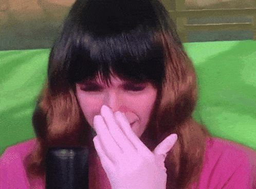 a woman wearing a wig and gloves is covering her nose