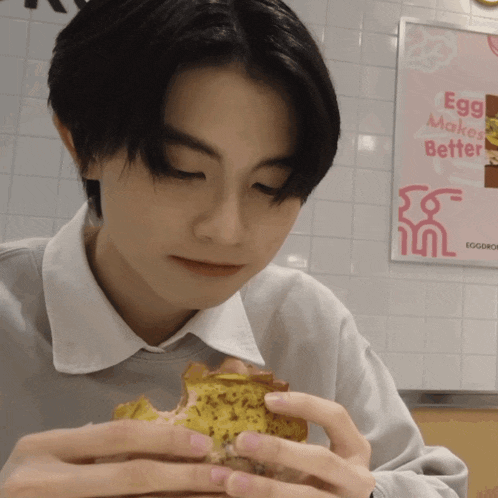 a person is eating a sandwich in front of a poster that says egg makes better