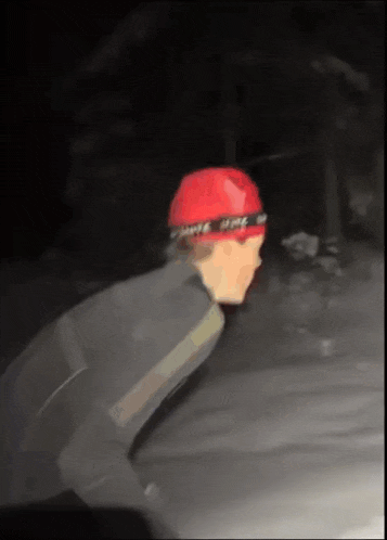 a man wearing a red hat and a black jacket is walking in the dark