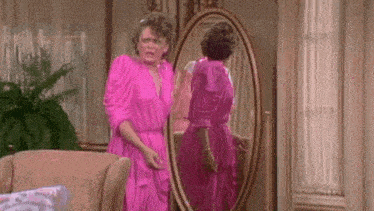 a woman in a pink dress is looking at herself in the mirror .