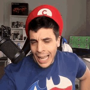 a man wearing a mario hat and a batman t-shirt is making a funny face .