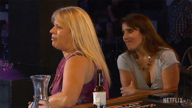 two women sit at a bar with a bottle of beer on the bar and a sign that says netflix