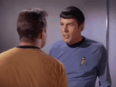 two men are standing next to each other and talking to each other . one of the men is wearing a yellow shirt .