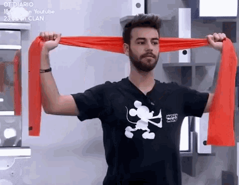 a man wearing a mickey mouse shirt is stretching his arms with an orange resistance band .