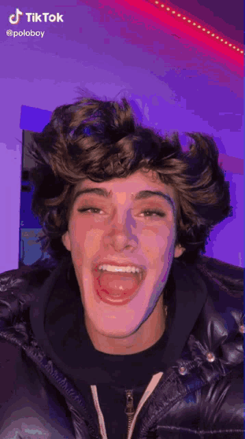 a young man in a black jacket is making a funny face with his tongue out .