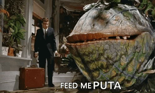 a man in a suit and tie is standing in front of a giant plant that says feed me puta