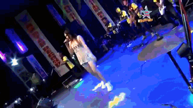 a woman singing into a microphone on a stage with a star on the bottom right corner
