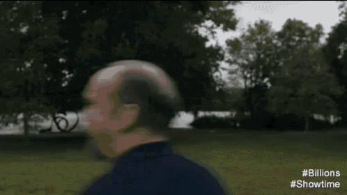 a man with a bald head is walking through a park .