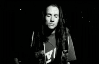 a black and white photo of a man with long hair standing in the dark .