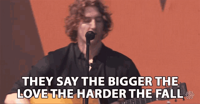 a man singing into a microphone with the words they say the bigger the love the harder the fall behind him