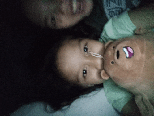 a little girl is laying next to a stuffed bear with a purple mouth