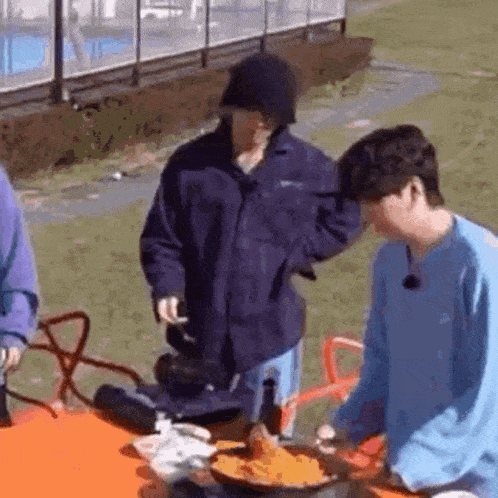 a group of young men are sitting at a table cooking food .