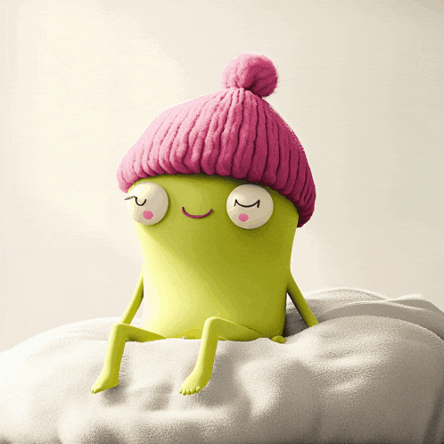 a green cartoon character wearing a pink hat is sitting on a pillow