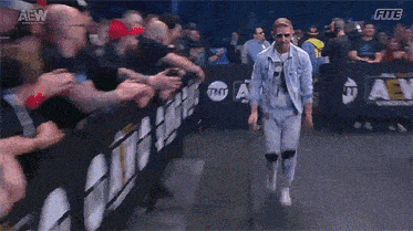 a man in a denim jacket is walking through a crowd of people in a stadium .