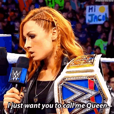 a woman is holding a wrestling championship belt and talking into a microphone while a crowd watches .
