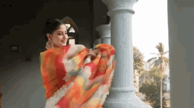 a woman wearing a colorful saree is standing next to a white pillar