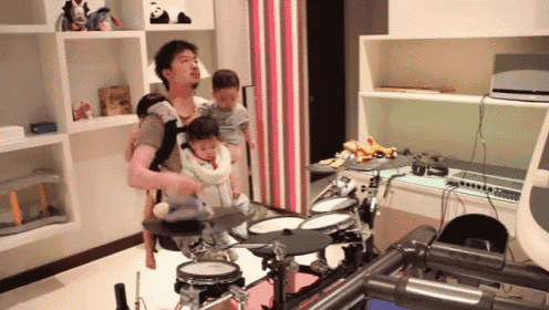 a man playing drums while holding a baby in a carrier