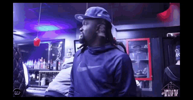 a man wearing a hat and a nike sweatshirt is standing in a dark room