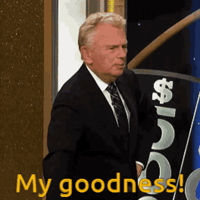 a man in a suit and tie is standing in front of a sign that says " my goodness "