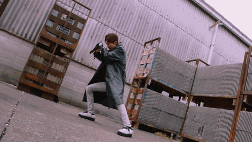 a man in a trench coat holding a gun in front of a building
