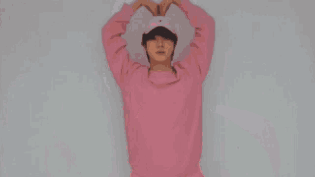 a man in a pink sweater and hat is making a heart with his hands .
