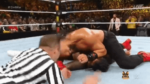 two men are wrestling in a wrestling ring and one of them is laying on the ground .