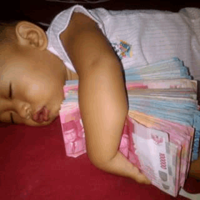 a baby is sleeping on a bed with a pile of money around his neck .