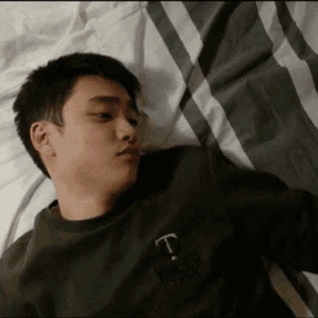 a young man laying on a bed wearing a green sweatshirt with the letter t on the front